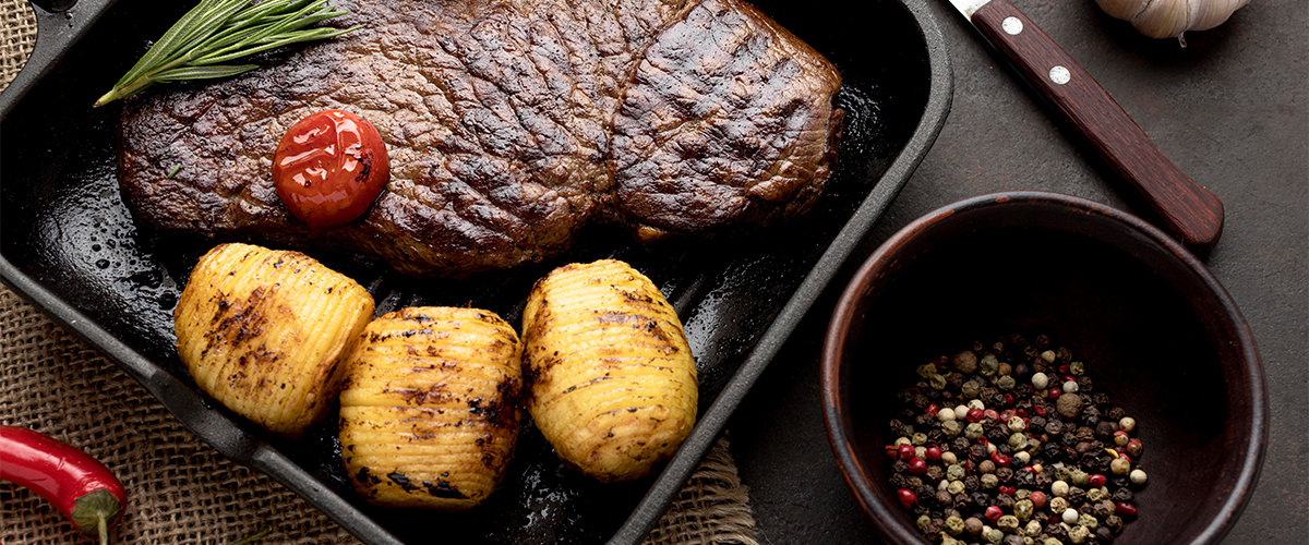 Steak, potatoes and garnish on a square grill pan